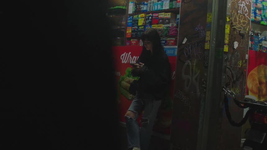Young woman using a cellphone next to a stall at night in the city