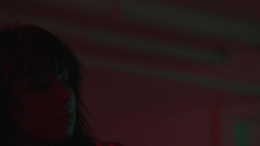 A woman with a bangs haircut and tattoos dances in red lighting