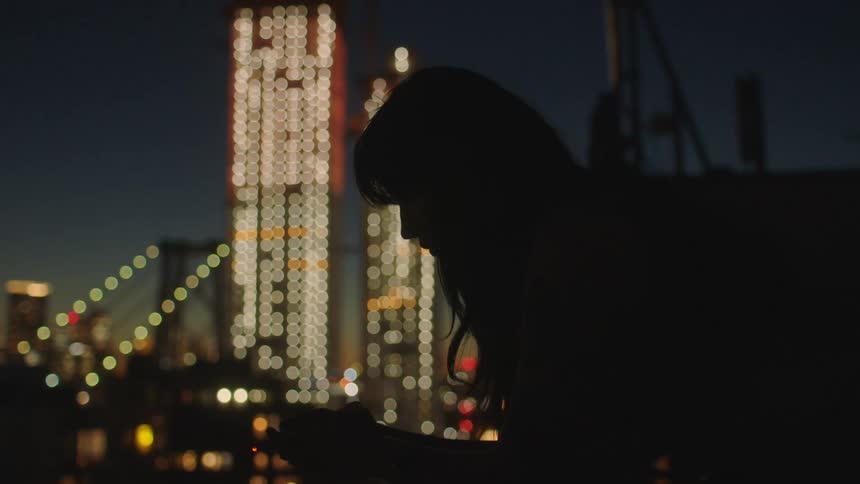 Silhouette of a young woman in front of the city skyline at night