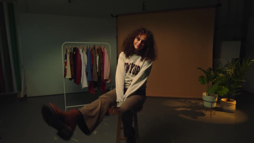 A girl sitting in a room with clothes hanging on the hanger
