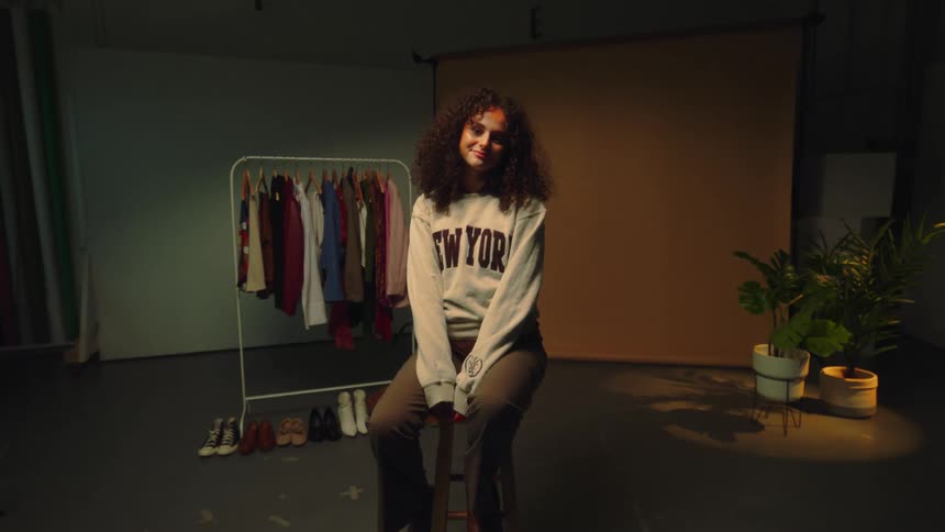 Woman sitting on a stool modeling with a slight smile and wearing a gray sweatshirt