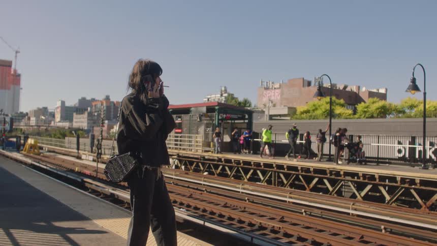 A young woman talks on her smartphone while waiting at a train stop on a summer day