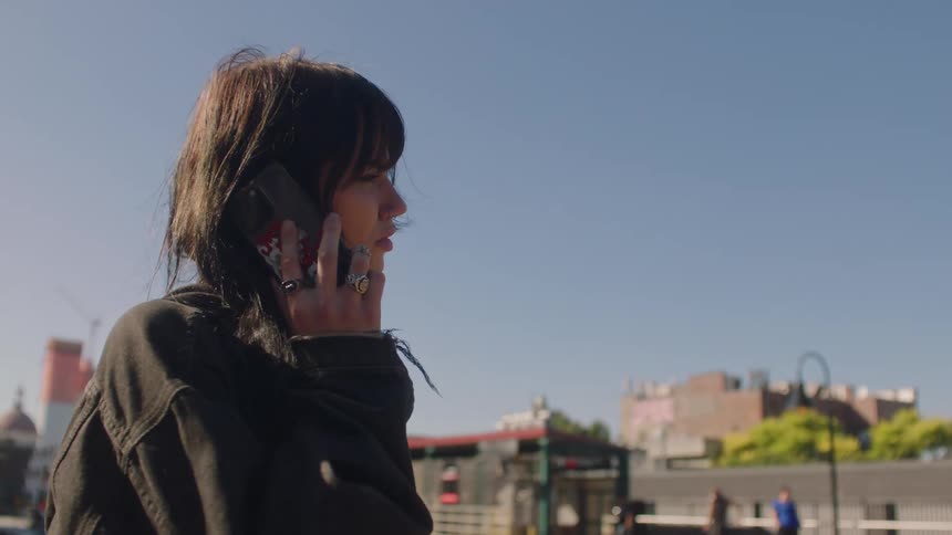 Woman makes phone call standing a distance from transit stop on sunny day
