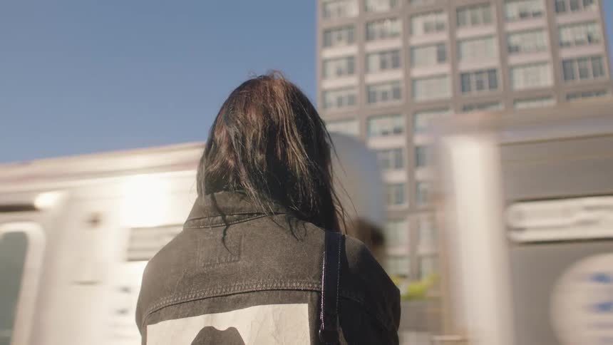A woman stands outside facing a train that is passing by her
