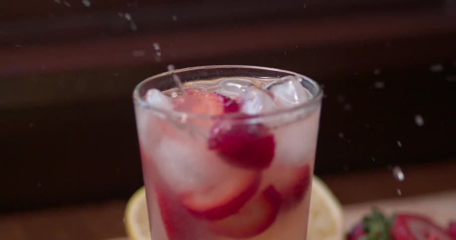 Pieces of strawberry are dropped in a full glass