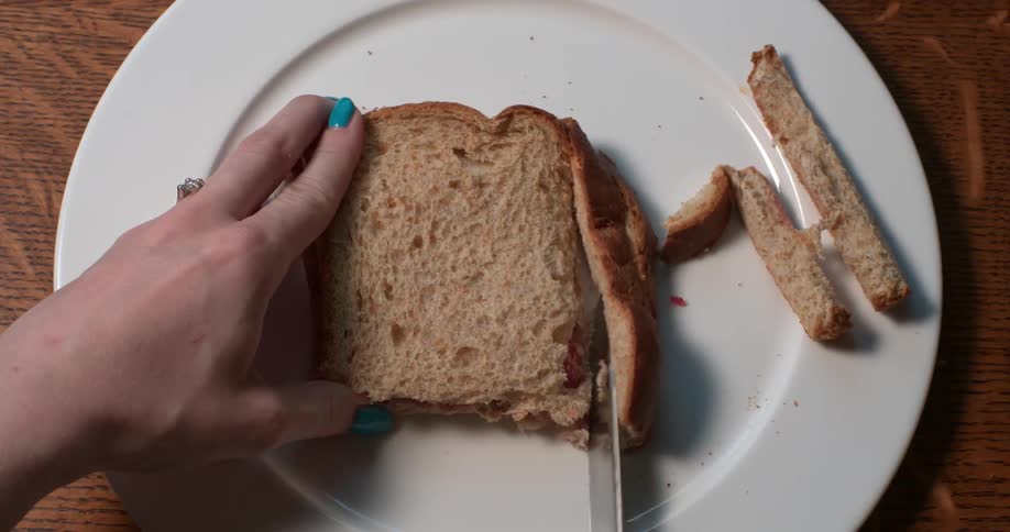 A person cuts the crust off a sandwich