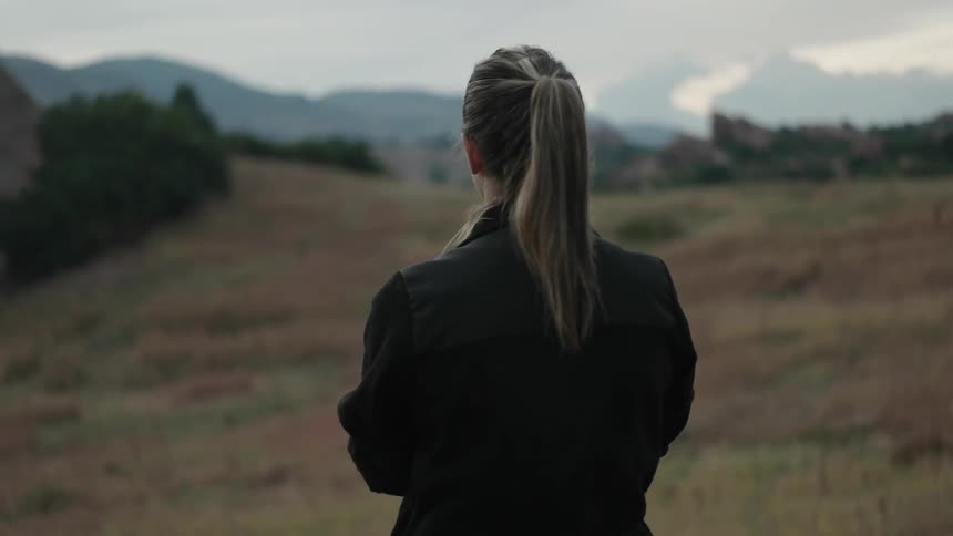 A woman looks out towards a field and mountains