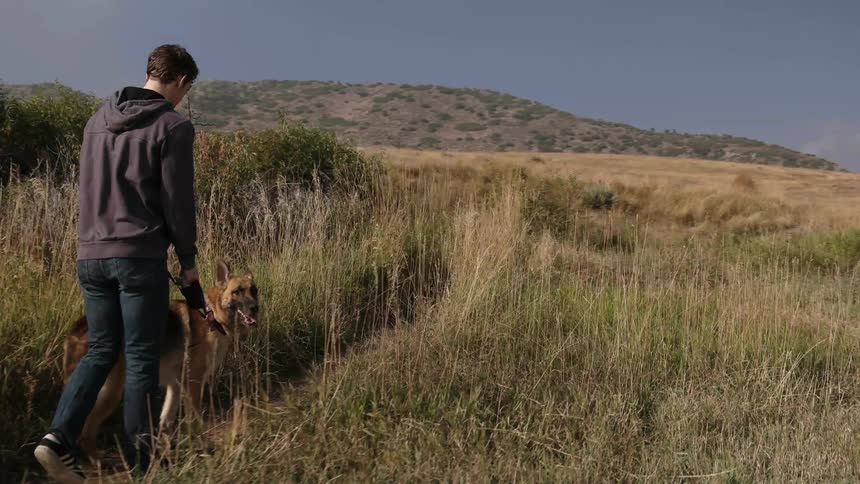 A man walks his dog down a small dirt path