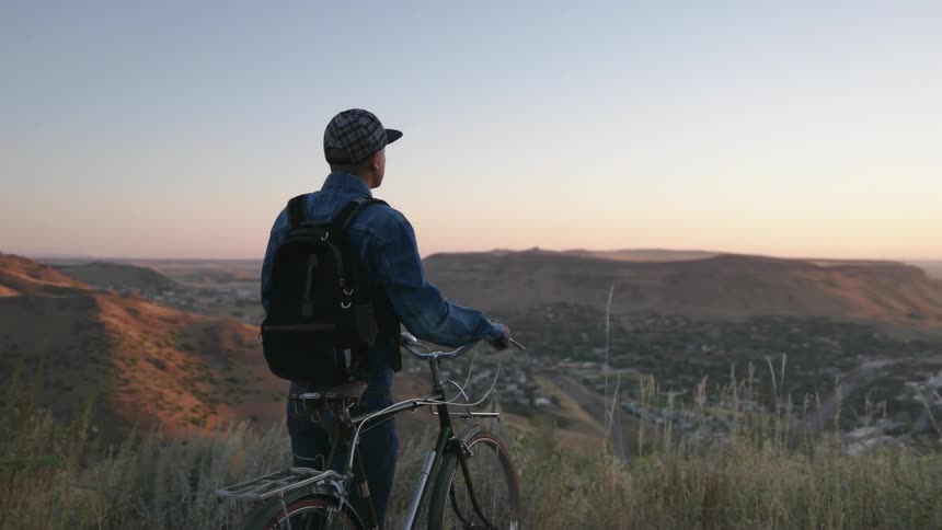 A man is standing next to his bicycle on a hilltop