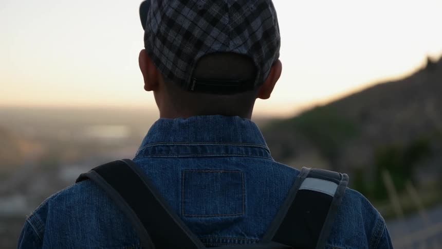 A man stands on a hill watching the sun set