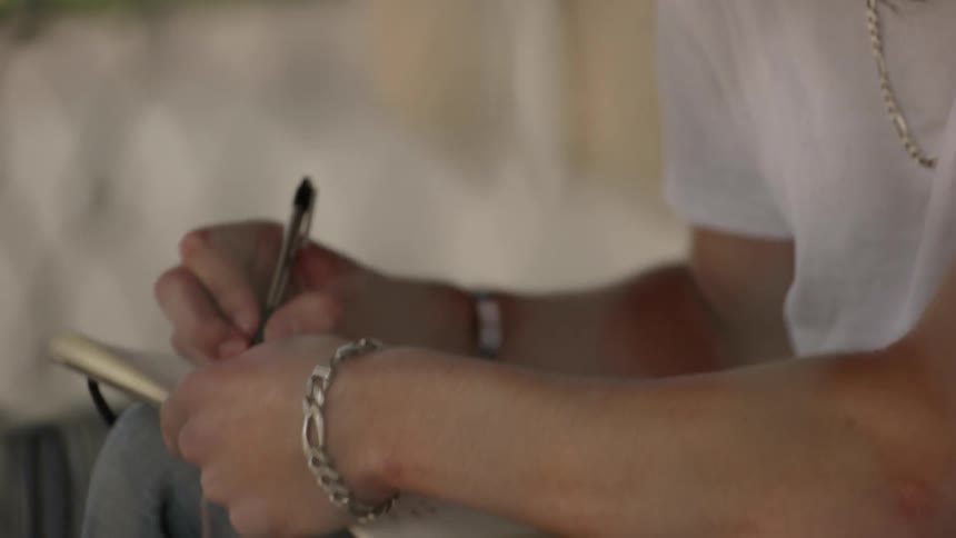 A man is looking down behind a fence writing in a book