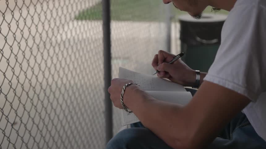 A man is sitting behind a fence writing