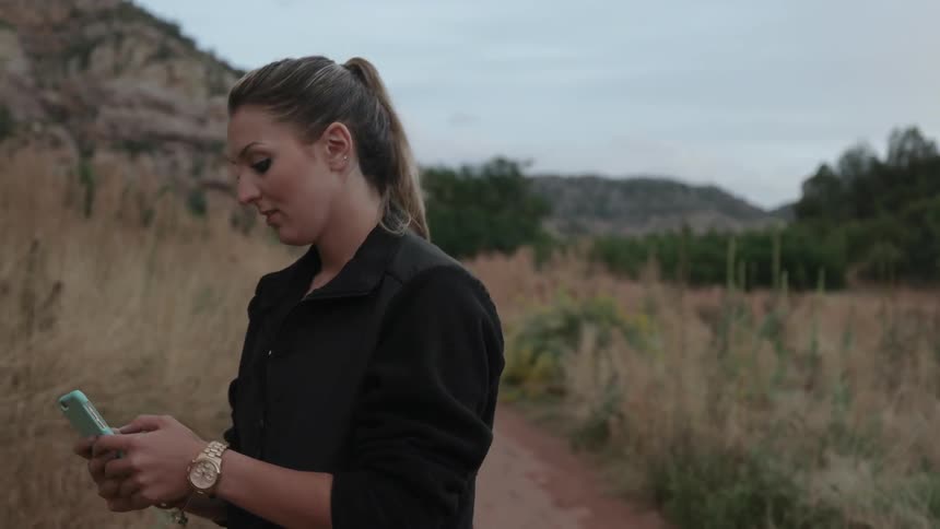 A woman walks along a field near a mountain