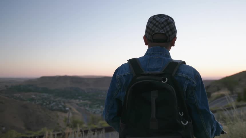 A man is on a hill looking at the sunset