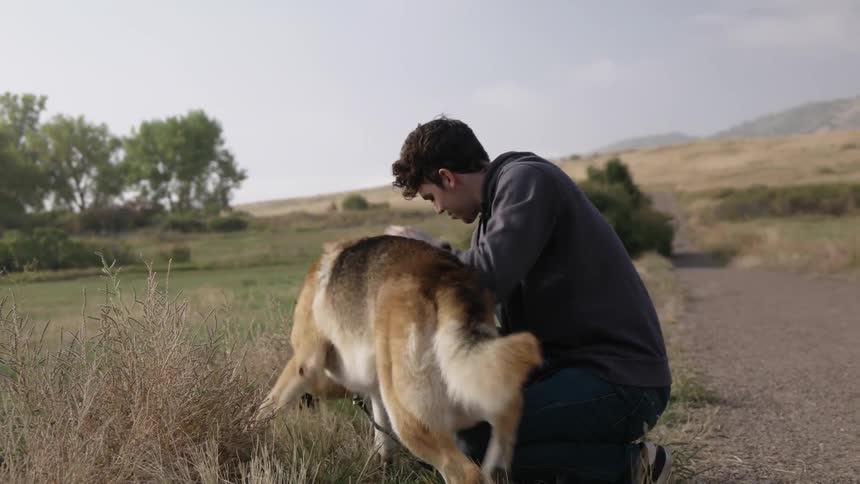 A man crouches down to pet his dog