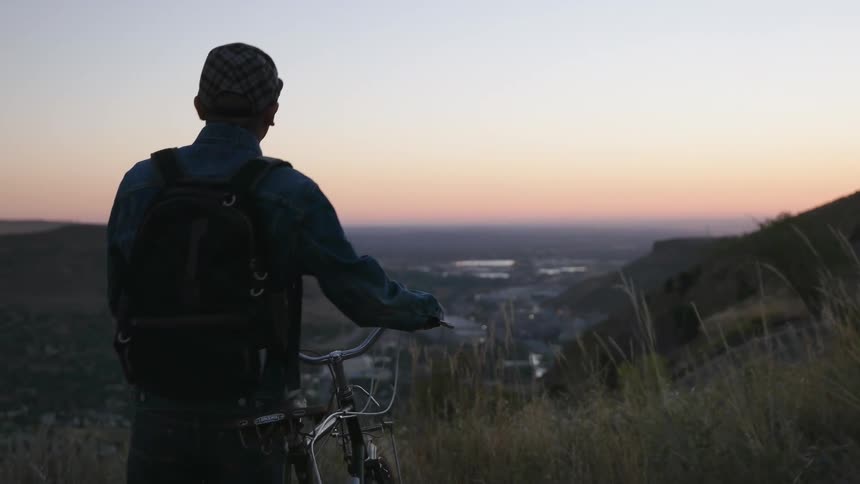 Man with a bicycle looks out over a valley at sunset
