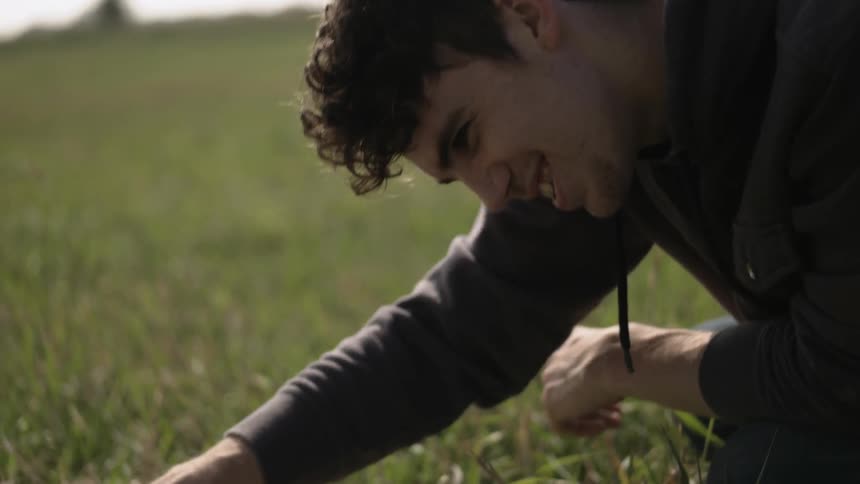 Man pets a dog laying in a grassy field