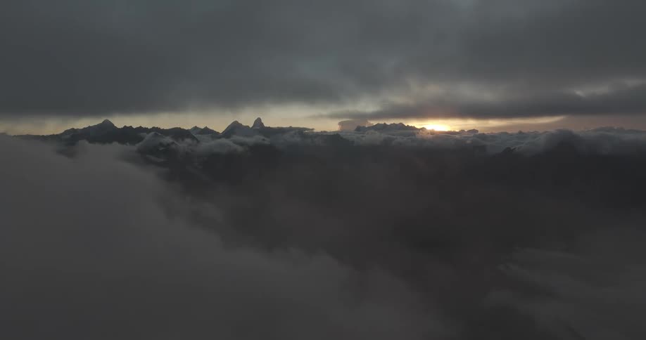 Aerial view of sun setting over the mountains between the clouds