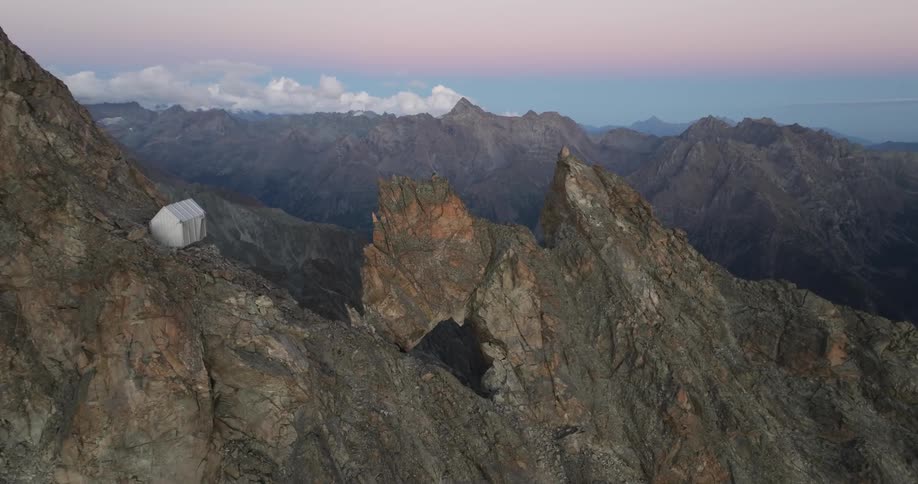 White tent perches on steep slope overlooking ridge with opening under a red tinted sky