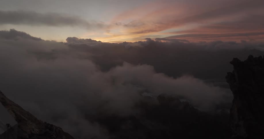 Aerial panorama of peaks and cliffs at cloud level with a reddish dawn sky