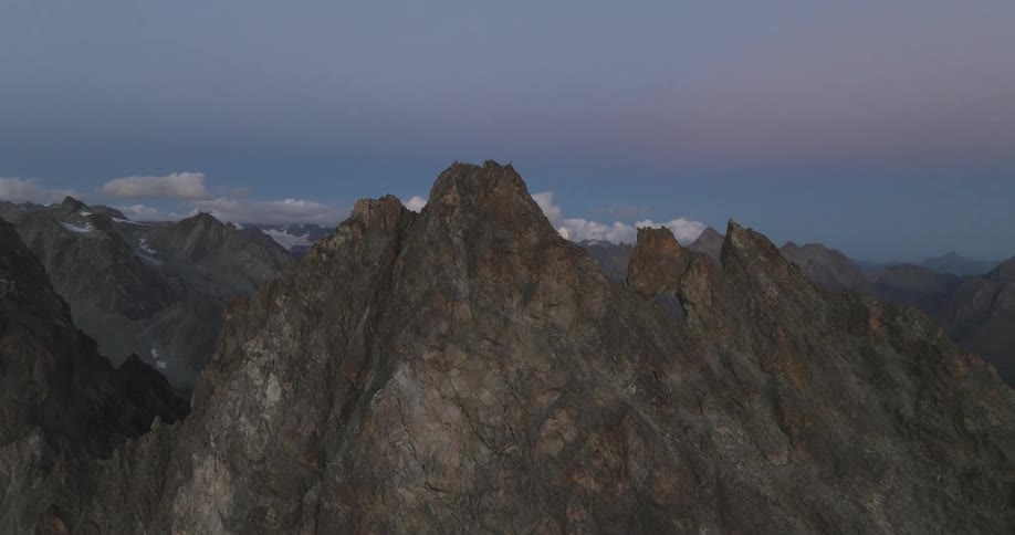 White tent perches on side of jagged mountain in range on a cloudy day