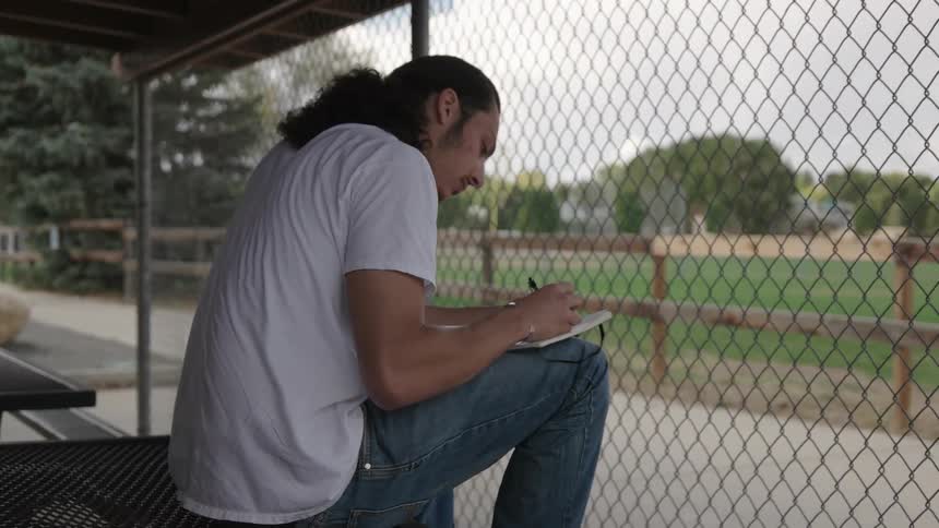 A man sits on a table behind a fence writing