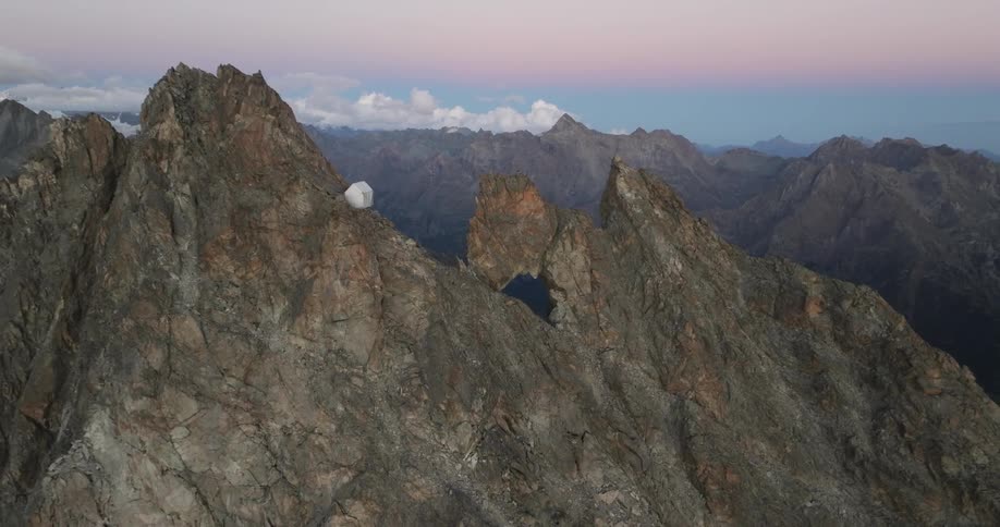 Camping tent amidst a cliff at the peak of a mountain on a day with a purple dawn sky