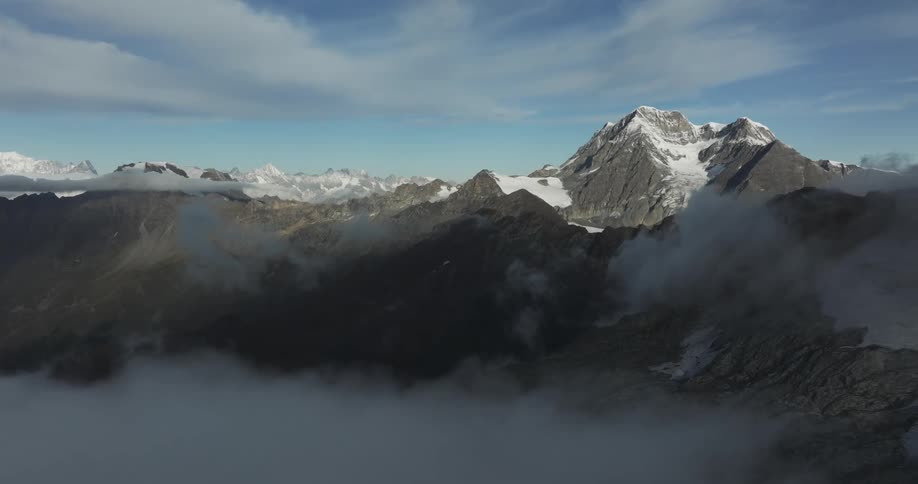 Aerial view of a high snowy mountain range towering above a sea of white clouds