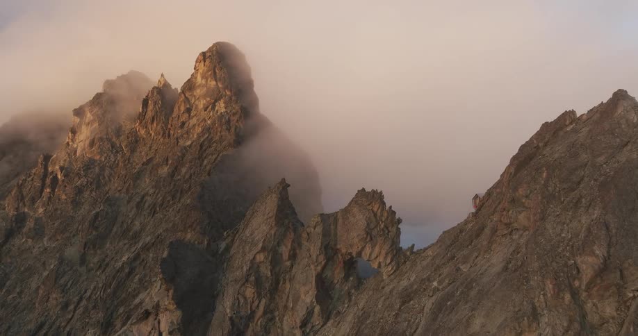 Aerial of a brown jagged rocky peak covered in a clouded fog at dawn