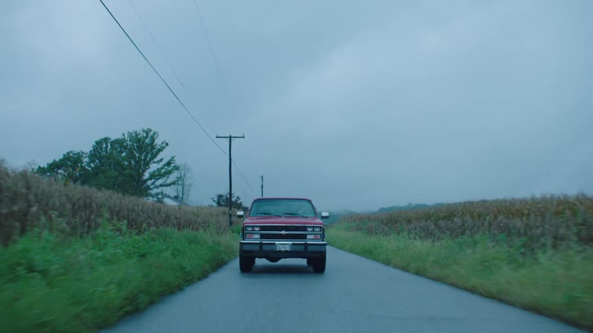 Red pickup truck driving on a narrow road with fields around