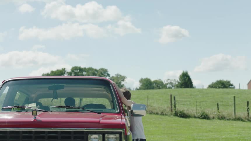 Man walking towards a pickup truck in the field and talking to another person inside
