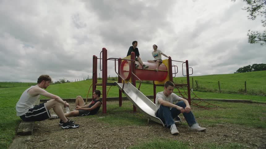Male friends sitting in a playground in the middle of a meadow