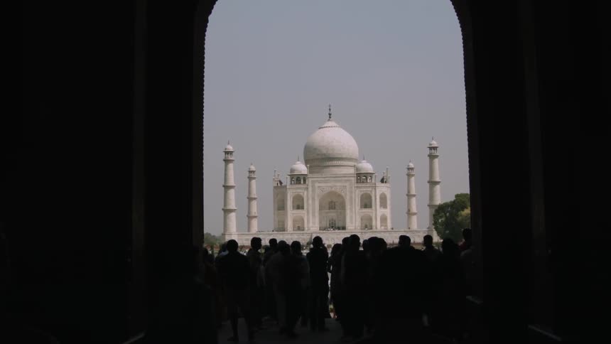 People stand in the shade of an arch before the Taj Mahal