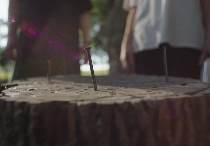 Two people stand next to a block of wood while a third person hammers a nail into it