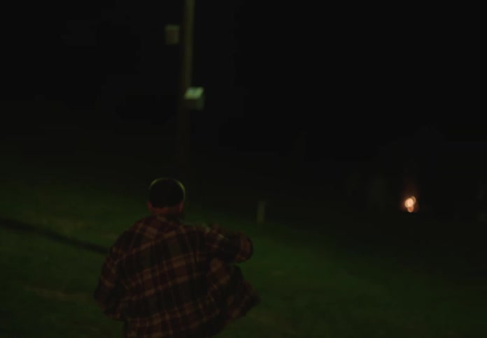 Boy walking at night putting on a jacket and heading towards a grassy area