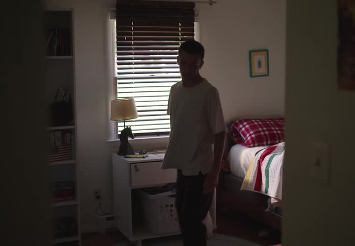 A teenage boy pick up a tshirt and put it on inside his bedroom