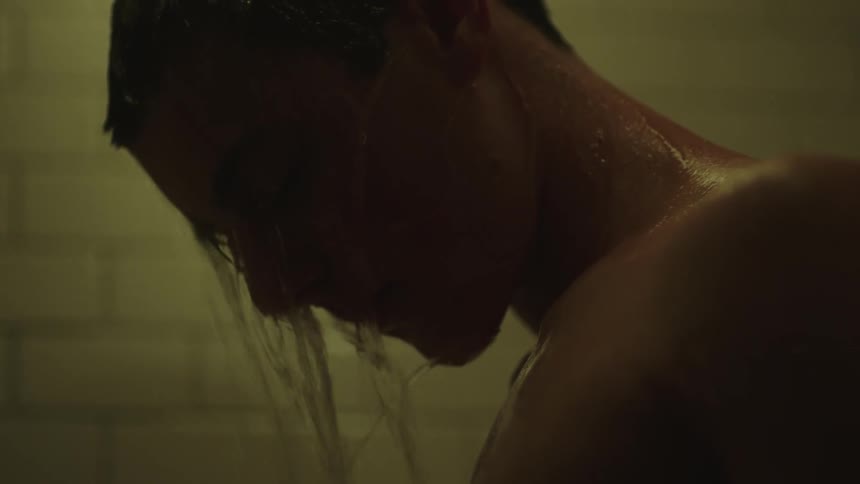 A young man hangs his head down as shower water runs down his face
