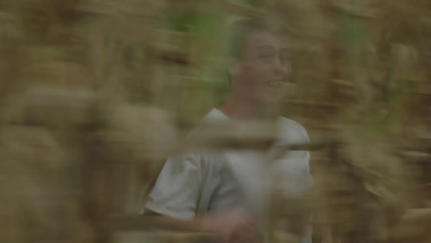 Man running at high speed in the middle of a cornfield with a facial expression of fear