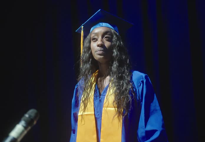 Woman greeting the graduate who is wearing a gown and starting to speak at the lectern