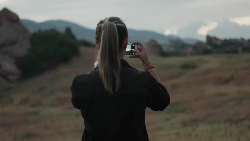 A person takes pictures of a mountain with her phone