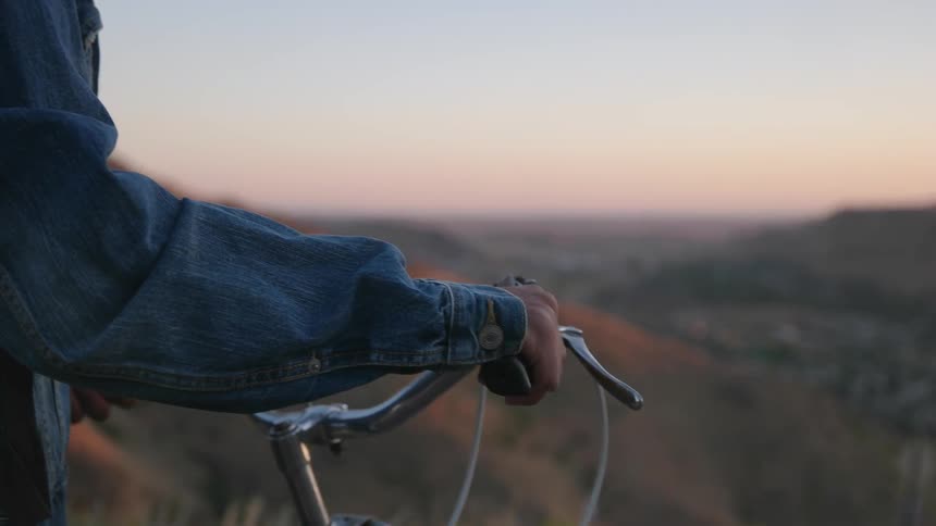Man on a bicycle looks out over a valley at sunset