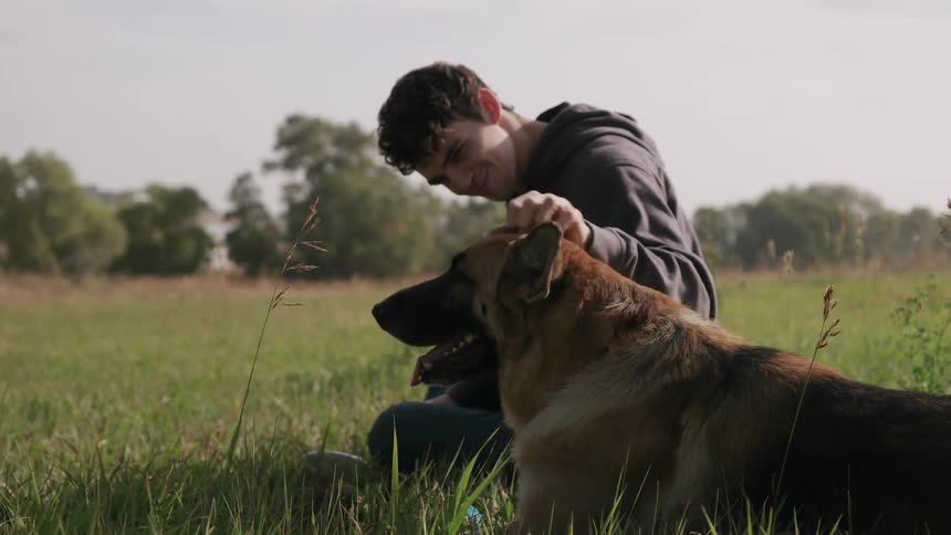 A man is sitting in the grass petting his dog