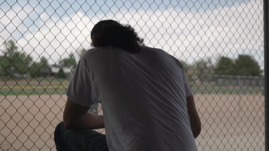 A man writes in a notebook by a fence