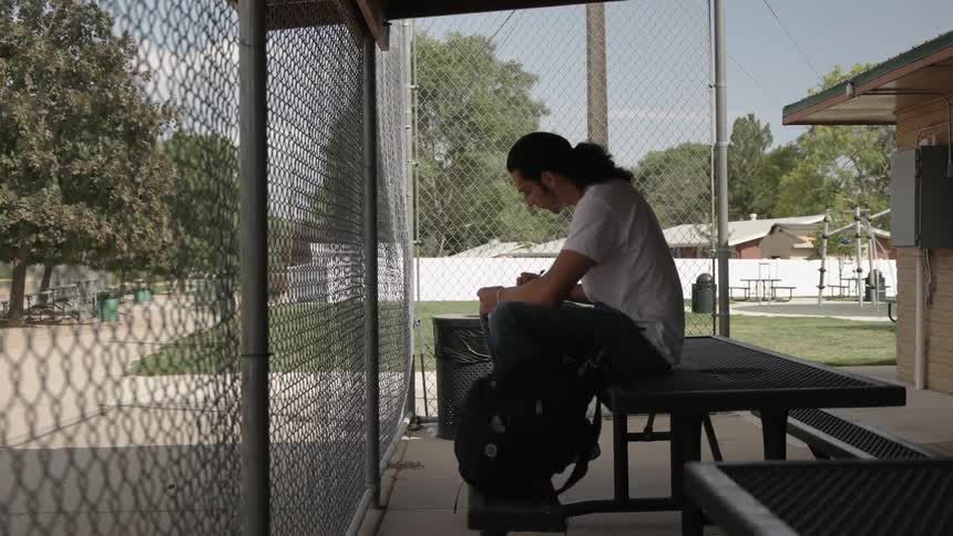 A man writes in a notebook while sitting on an outdoor picnic table