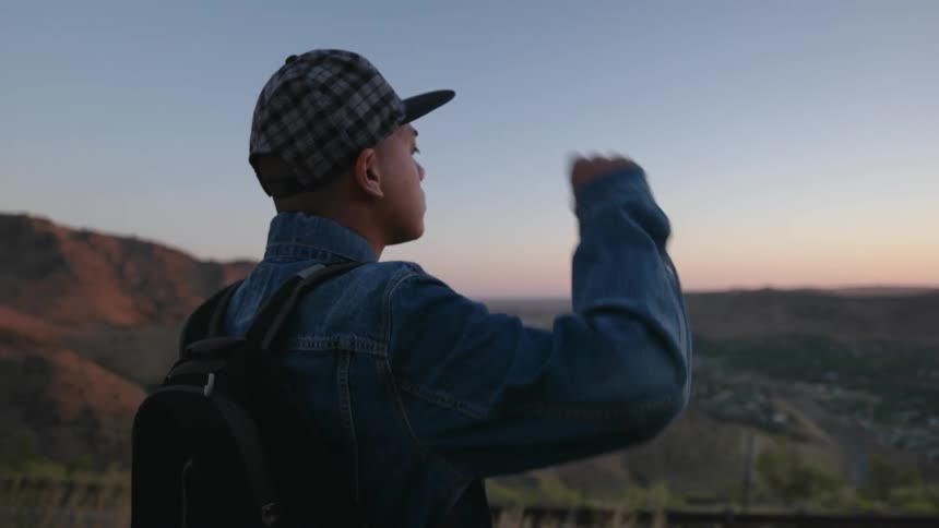 A man looks over a horizon at sunset and adjusts his hat