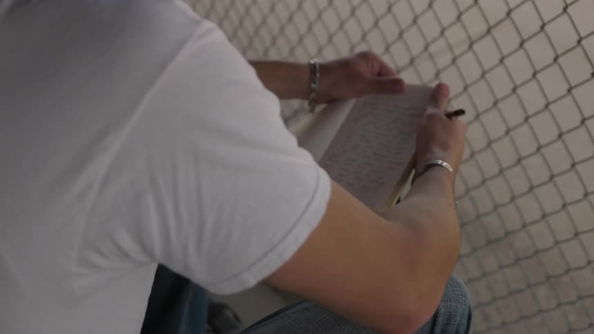 A man writes in a notebook by a fence