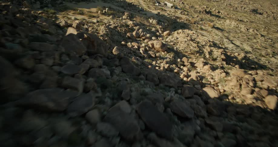 Vehicles park near rough mountainous terrainand near a farm with pasture land
