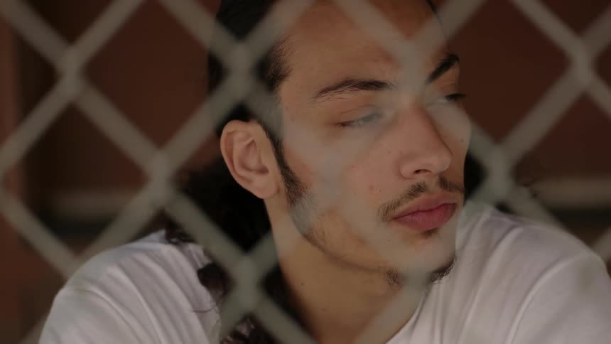 Man sits behind a chain link fence and looks around