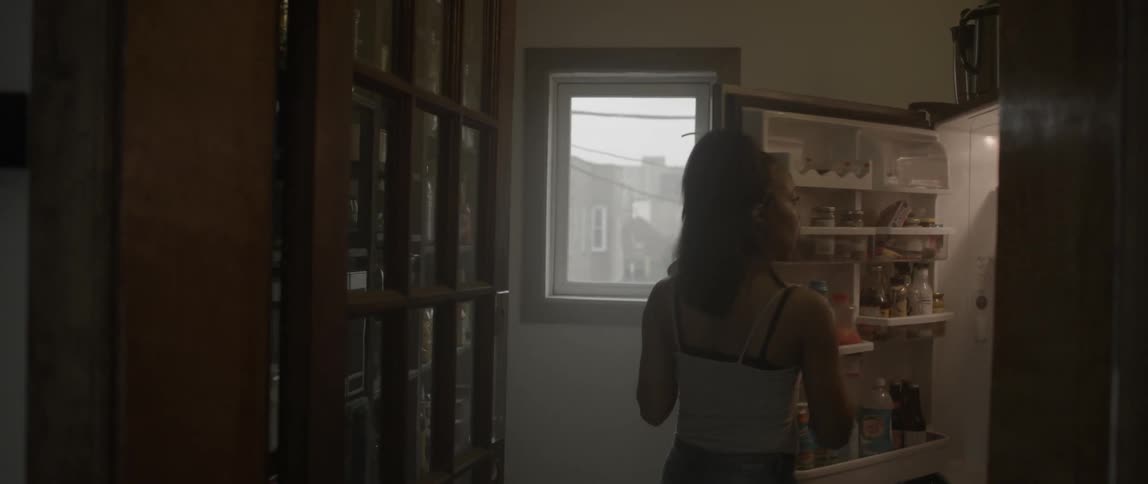 A woman grabs some food from the fridge and walks off