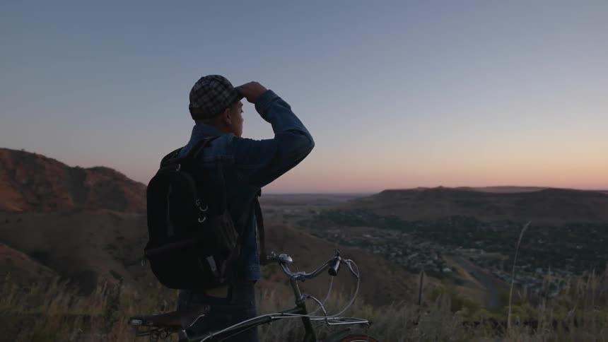 A man walks his bicycle to the edge of a hill